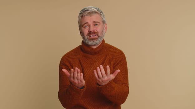 Senior middle-aged man feeling hopelessness loneliness, nervous breakdown, loses becoming surprised by lottery results, bad fortune, loss, unlucky news. Mature guy isolated on studio beige background