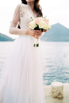 Bouquet of flowers in the hands of the bride on the pier by the sea. High quality photo