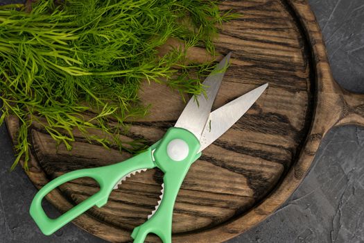 kitchen scissors cutting dill in the kitchen on a cutting board in the kitchen. Close-up of kitchen accessories. cooking. Fresh greens. Healthy eating.