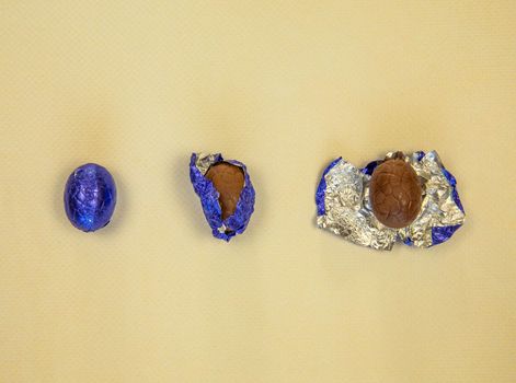 Chocolate Easter eggs wrapped in shiny blue foil yellow background, flat lay top view, with copy space Happy Easter concept sweet candy snack