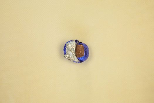 Chocolate Easter eggs wrapped in shiny blue foil yellow background, flat lay top view, with copy space Happy Easter concept sweet candy snack