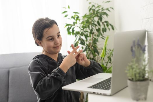 A teenage girl sits in front of her laptop learning sign language, a language for the deaf online.