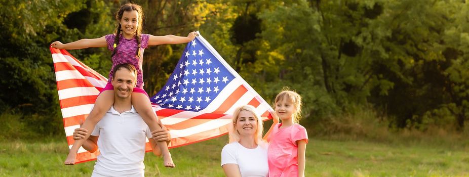 Happy family sitting together in their backyard holding the american flag behind them. Smiling couple with their kids celebrating american independence day holding american flag.