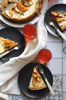 Portions of ginger tart with fresh peach slices on black plates. Tart cut into portions with crumbs. Berry juice in glass glasses.