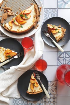 Portions of ginger tart with fresh peach slices on black plates. Tart cut into portions with crumbs. Berry juice in glass glasses.