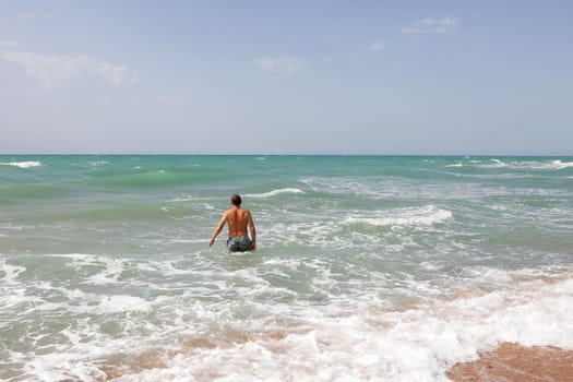 man enters the sea to swim. Moderate waves on the sea, sandy beach.