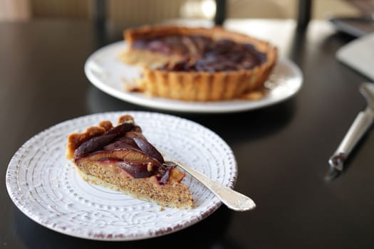 piece of plum and almond tart with frangipane on a white plate. selective focus.