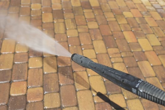 Washing paving slabs with a high pressure washer. Spring cleaning. Man in a navy blue uniform cleans dirt from paving slabs with a pressure washer