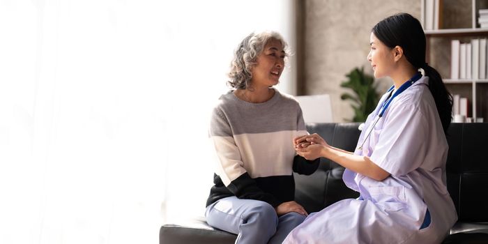 Home caregiver and senior woman holding hands. Professional Elderly Care. Professional care for elderly at nursing homes. Nurse holding hand of senior woman in rest home.