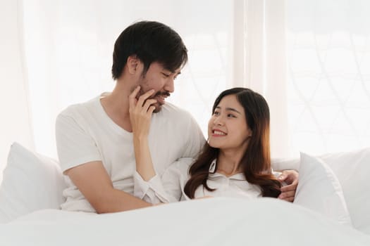 Asian couple lying in bed in a home, anniversary or romance. Intimacy, happy while on romantic vacation, trip.