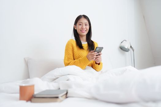 Asian woman texting on her mobile phone in the bedroom at home. messaging or browsing social networks while relaxing concept