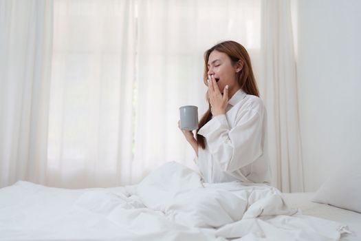 Beautiful asian woman has woken up on a white bed and holding coffee in the morning at home. lifestyle concept