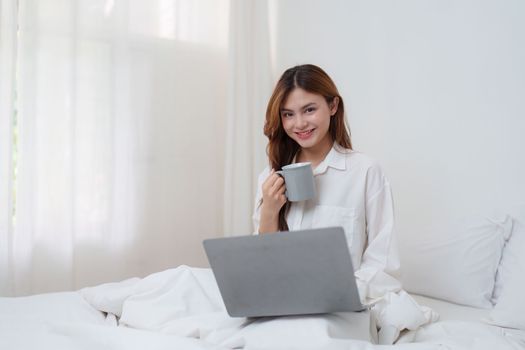 Beautiful asian woman has woken up on a white bed and holding coffee in the morning at home. lifestyle concept.