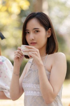 Young asian woman drinking coffee or tea on picnic at outdoor park