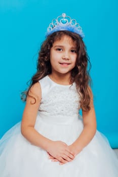 girl in a white dress with a crown on her head for a holiday on a blue background