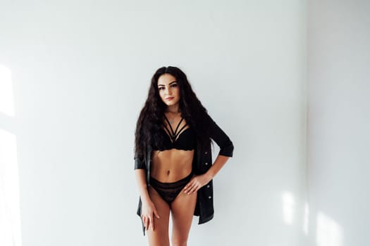 brunette woman in black underwear stands against a white wall