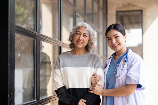 Young caregiver helping senior woman walking. Nurse assisting her old woman patient at nursing home. Senior woman with walking stick being helped by nurse at home..