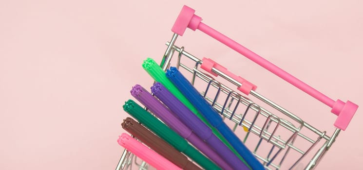 Creative learning and creativity concept with shopping cart with markers on pink background, copy space.