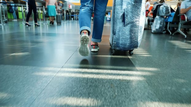 close-up. back view. female legs in sneakers. Woman, Traveler, passenger with her wrapped suitcase, luggage walking through the hall of Airport. High quality photo