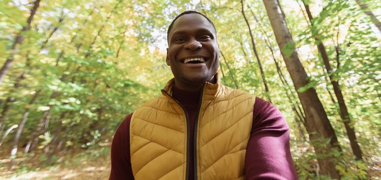 African American man taking a self portrait with a smartphone in autumn fall park. Happy people, season and new normality