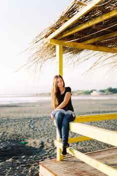 Young woman sits on the railing of a wooden house on the beach. High quality photo