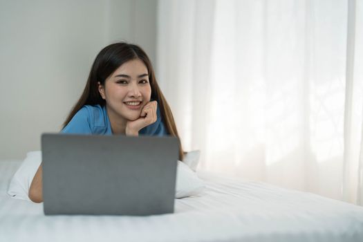 Happy, Relaxing Young beautiful Asian female watching movie or series on notebook in emotional smile happily while laying on the bed in her bedroom. Day off, Chill out and leisure concept...