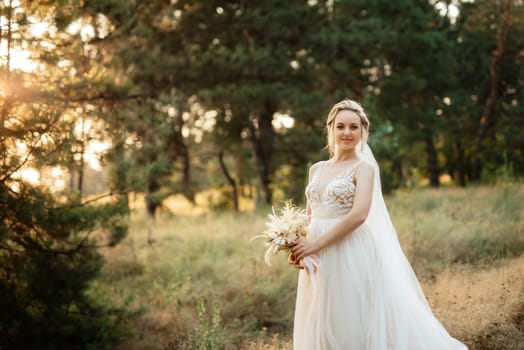 bride blonde girl with a bouquet in the forest in the sunset light