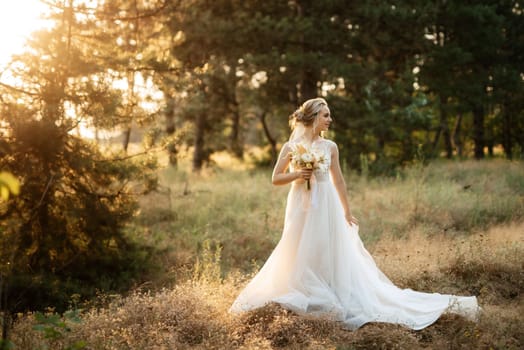 bride blonde girl with a bouquet in the forest in the sunset light