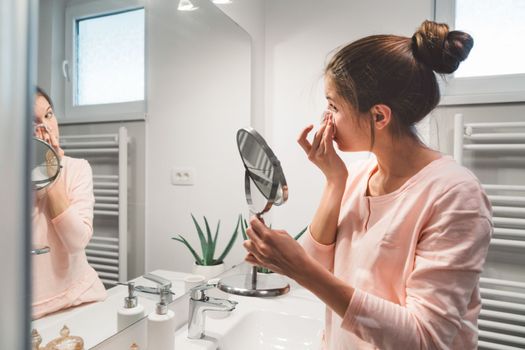 Young caucasian woman getting ready in a bright white modern bathroom. Woman doing her skincare, cleaning her face, teeth and body int he bathroom.