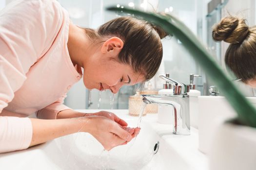 Young caucasian woman getting ready in a bright white modern bathroom. Woman doing her skincare, cleaning her face, teeth and body int he bathroom.