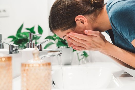 Young caucasian woman getting ready in a bright white modern bathroom. Woman doing her skincare, cleaning her face, teeth and body int he bathroom.