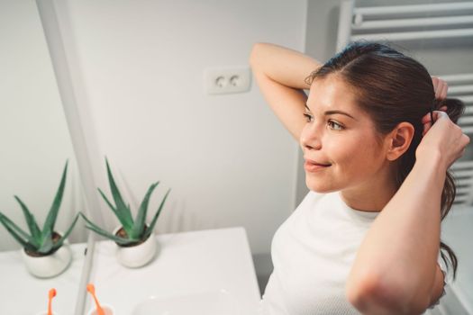 Young caucasian woman getting ready in a bright white modern bathroom. Woman doing her skincare, cleaning her face, teeth and body int he bathroom.