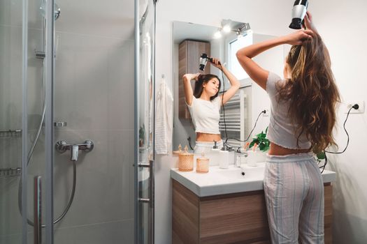 Young caucasian woman getting ready in a bright white modern bathroom. Woman doing her skincare, cleaning her face, teeth and body int he bathroom.