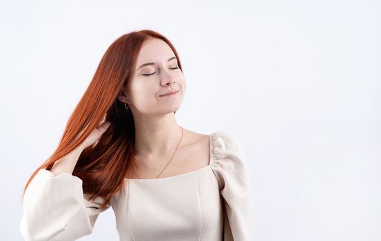 Happy beautiful woman smiling with closed eyes touching her red straight hair over white background, copy space