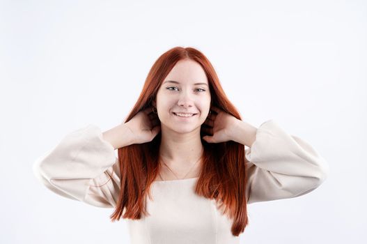 Happy beautiful woman smiling with closed eyes touching her red straight hair over white background, copy space