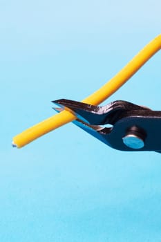 Blue wire cutter cuts yellow wire on blue background close up