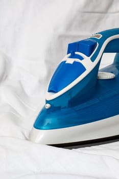 Blue iron on a white sheet, ironing, copy space