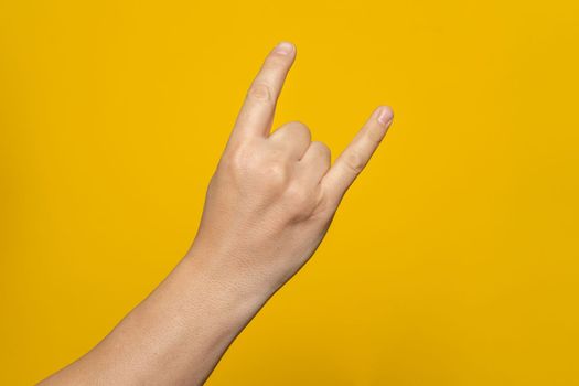 Male hand close-up on a yellow background shows hand gesture. Rock'n'roll. Isolate.