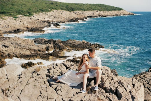 Man and woman sit on rocks near turquoise water. High quality photo