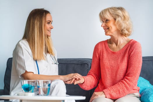Young blonde woman caregiver helping senior woman at home. Nurse assisting her old woman patient at nursing home. Senior woman being helped by nurse at home. High quality photo
