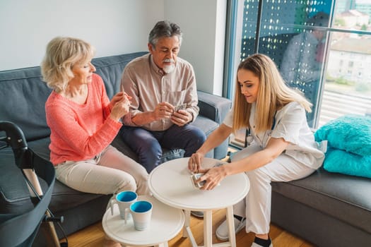 Young blonde woman caregiver helping senior married couple at home. Nurse assisting her senior patients at nursing home. Senior couple being helped by nurse at home. High quality photo