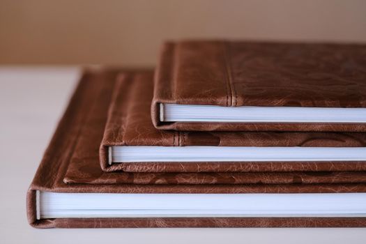 Composition of photo books in natural brown leather of different sizes. Fragment of a photobook binding.