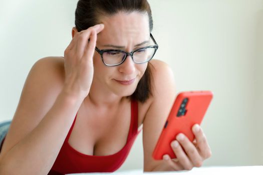 Woman talk via a smartphone video camera with look of problem on her face while lying on bed.