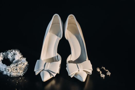 white wedding shoes and garter belt with earrings on a black background.
