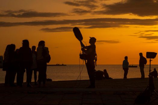TRIESTE, ITALY - APRIL, 17: Behind the scene. Sound recorder with microphone, boom mic and headphones together the film crew team filming movie scene on outdoor location at sunset on April 17, 2018