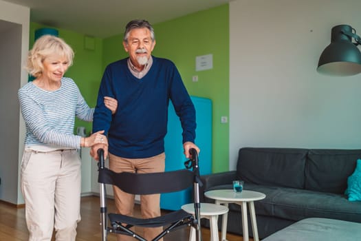 Senior woman helping senior man walking inside the apartment at home. High quality photo