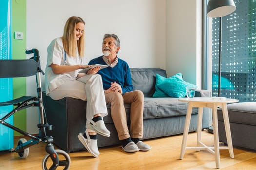 Young blonde woman caregiver helping senior man at home. Nurse assisting her old man patient at nursing home. Senior man being helped by nurse at home. High quality photo