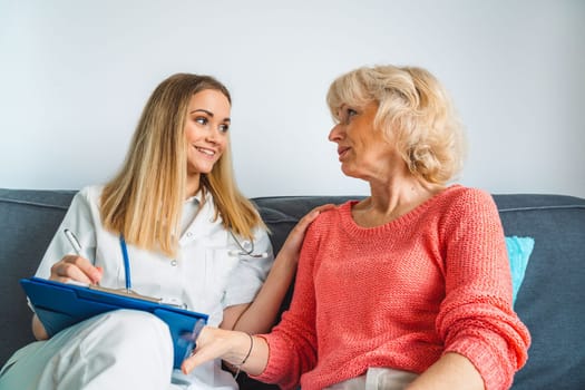 Young blonde woman caregiver helping senior woman at home. Nurse assisting her old woman patient at nursing home. Senior woman being helped by nurse at home. High quality photo