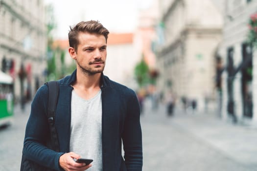 Beautiful caucasian man living in the city. Man spending his day in the city, sun is shining, weather is nice. Young millennial person living in the city, doing his daily errands always using his digital devices, tablet or phone.