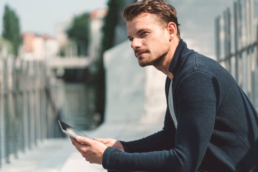 Beautiful caucasian man living in the city. Man spending his day in the city, sun is shining, weather is nice. Young millennial person living in the city, doing his daily errands always using his digital devices, tablet or phone.